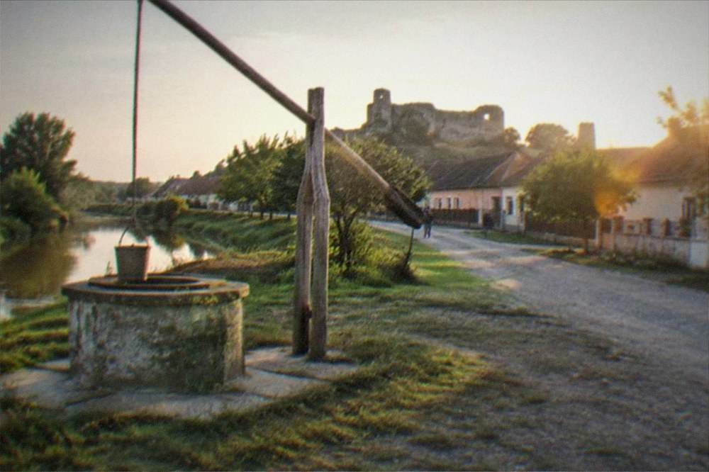A village well with a wooden shadoof frame beside a gravel road