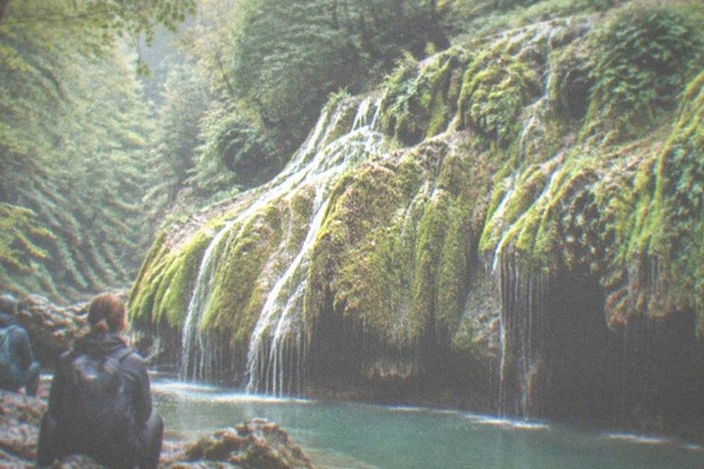 Hikers with backpacks resting on rocks beside a turquoise river pool