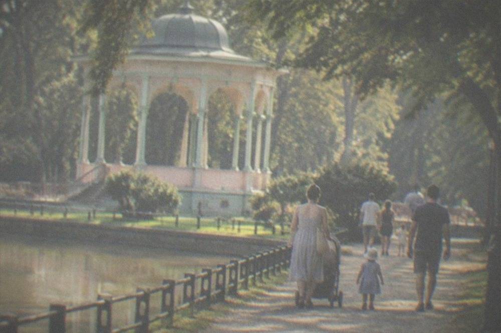 Families strolling on a gravel path beneath mature trees in a spa park