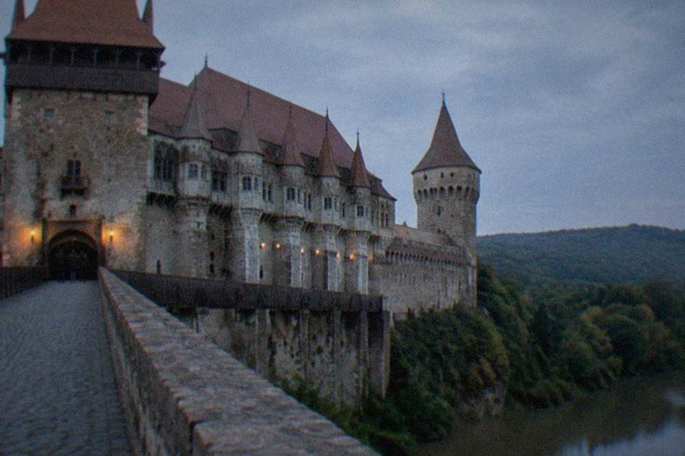 A stone footbridge leading to a fortified castle gate with pointed towers above