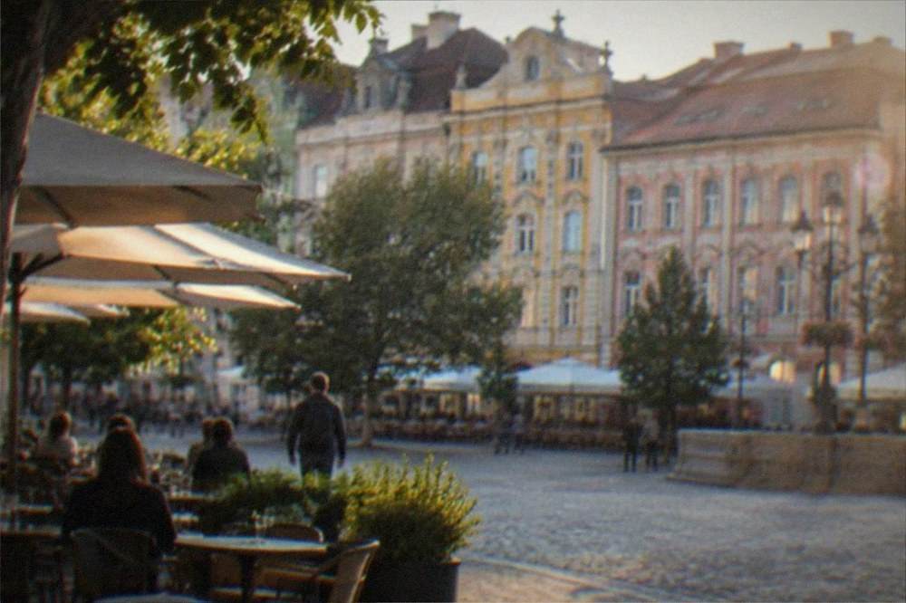 An old town square lined with colorful baroque buildings and outdoor cafe tables