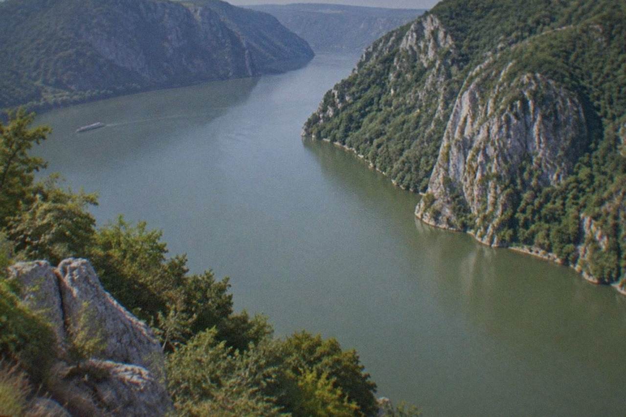 Steep rocky cliffs rising on both sides of a wide river bend with forested slopes and calm water below