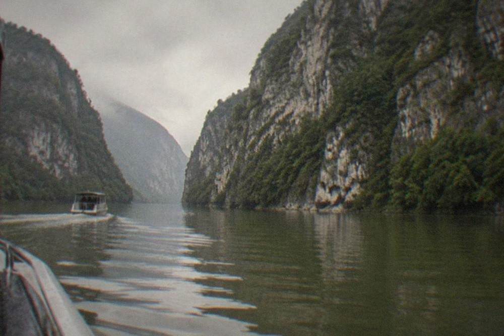 A small boat moving through a narrow river channel with high stone cliffs reflected in the water