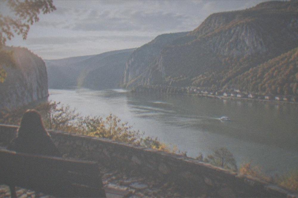 Autumn colors on steep forested slopes above a calm blue river with a small village on the far shore