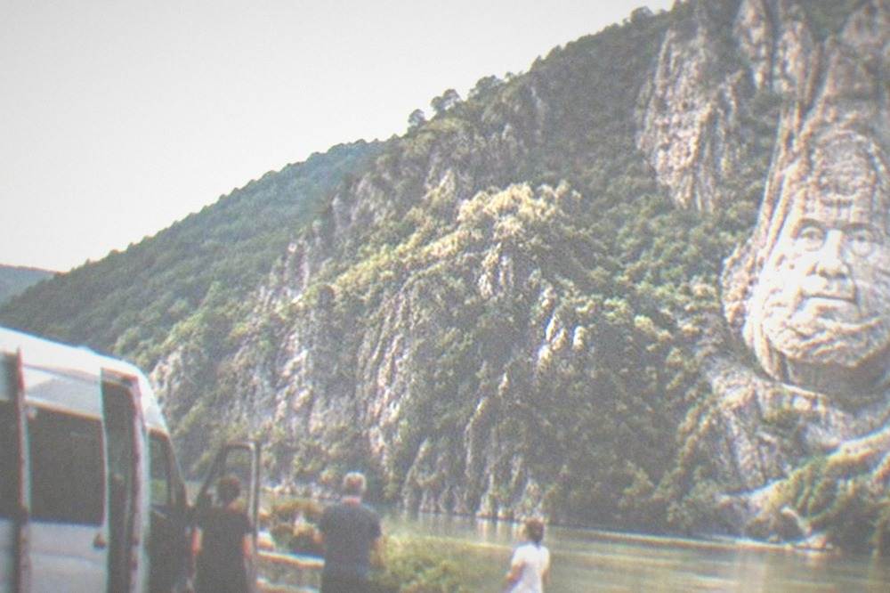 A tour van parked at a riverside viewpoint with cliffs rising behind it