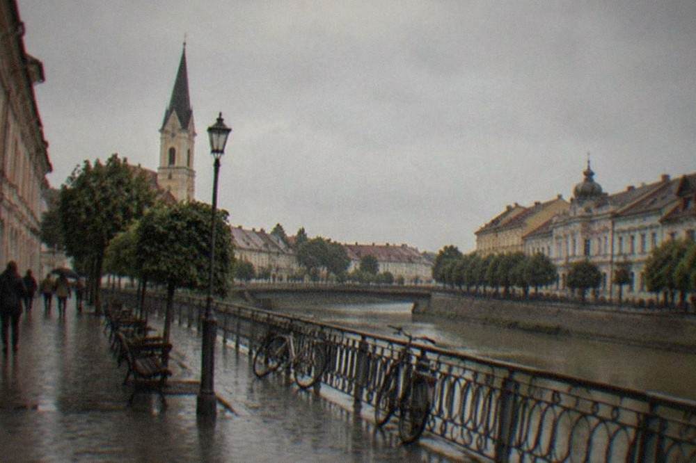 A quiet town square with pastel facades, parked bicycles and a few people walking