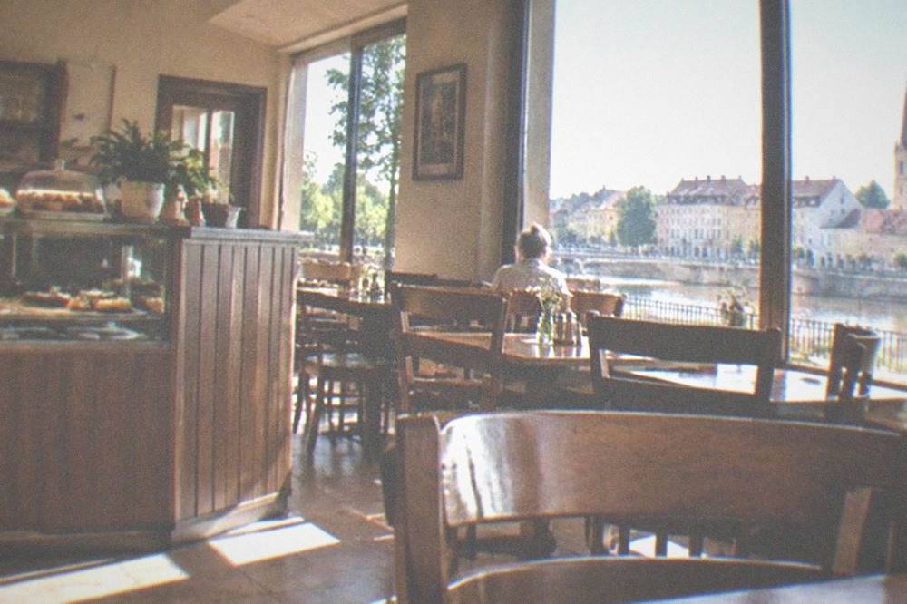 A simple neighborhood restaurant interior with wooden tables, chairs and a counter with pastries