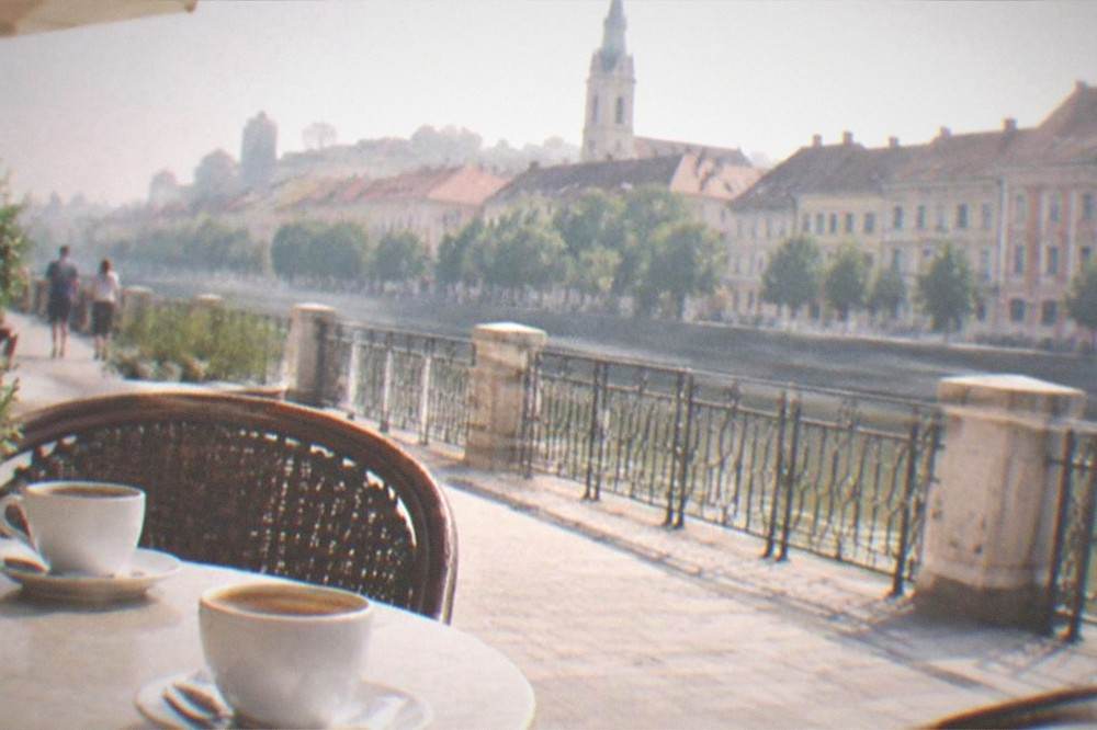 A cafe table on a pedestrian street with coffee cups and a receipt, morning sun on old facades