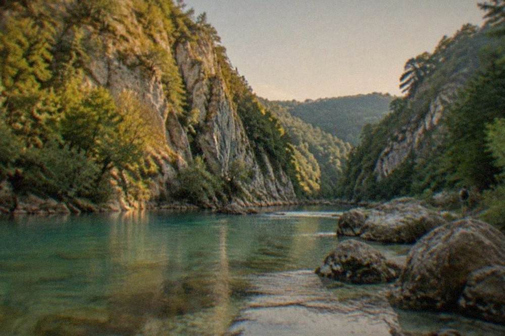Clear turquoise water flowing over a rocky riverbed inside a forested canyon