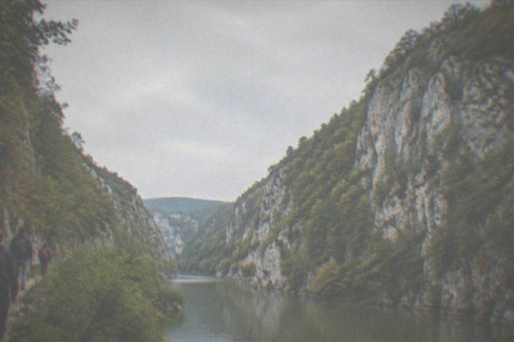 Hikers on a narrow trail beside a river between high rock walls