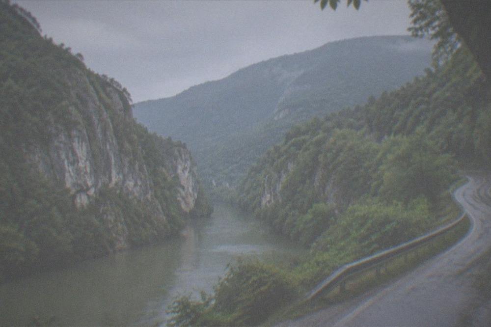 A winding country road through green hills toward forested mountains