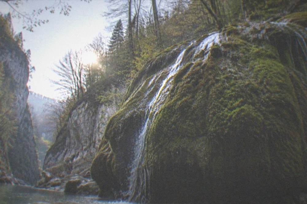 A thin sheet of water folding over a moss covered rock dome in a forest