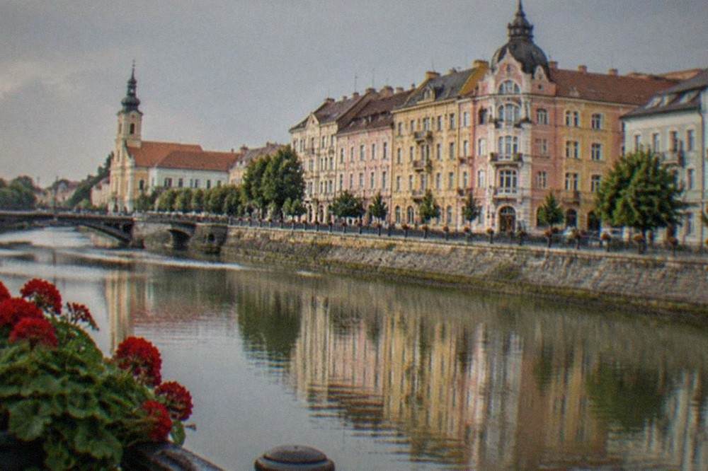 A river reflecting colorful restored buildings along an Oradea embankment