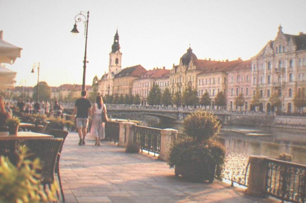 A sunny pedestrian square with cafe tables and people strolling past ornate buildings