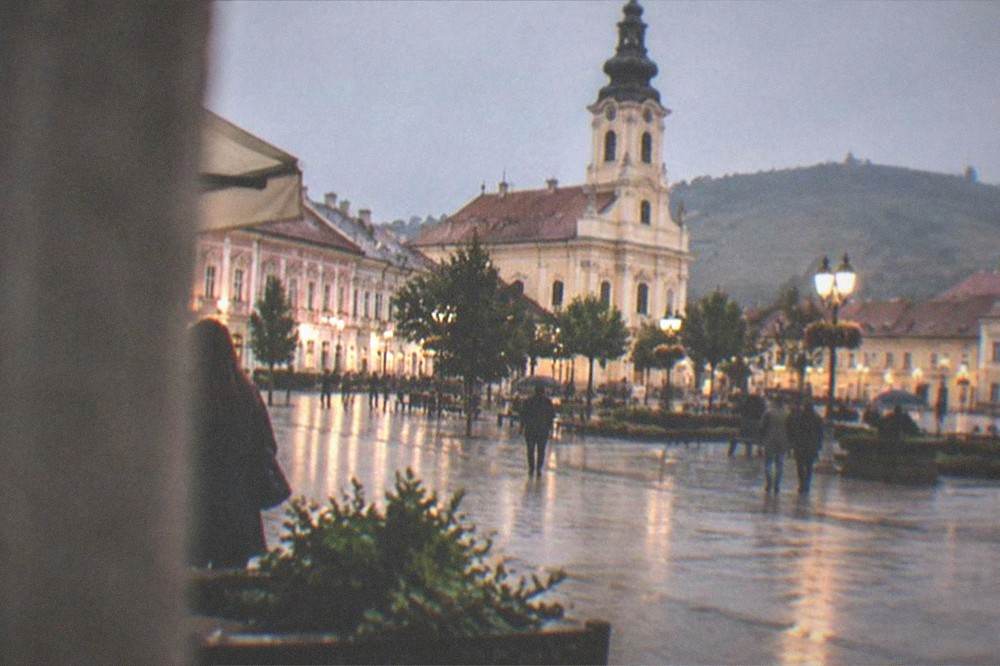 A town square at dusk with lit facades and people walking