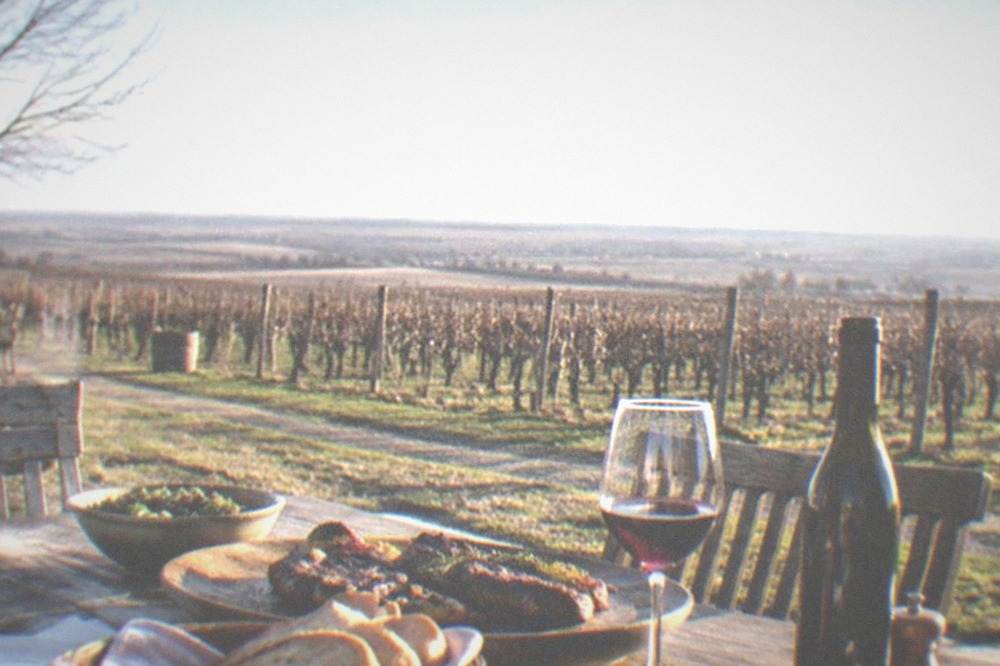 A rustic restaurant table set with grilled meat, bread and a bottle of red wine