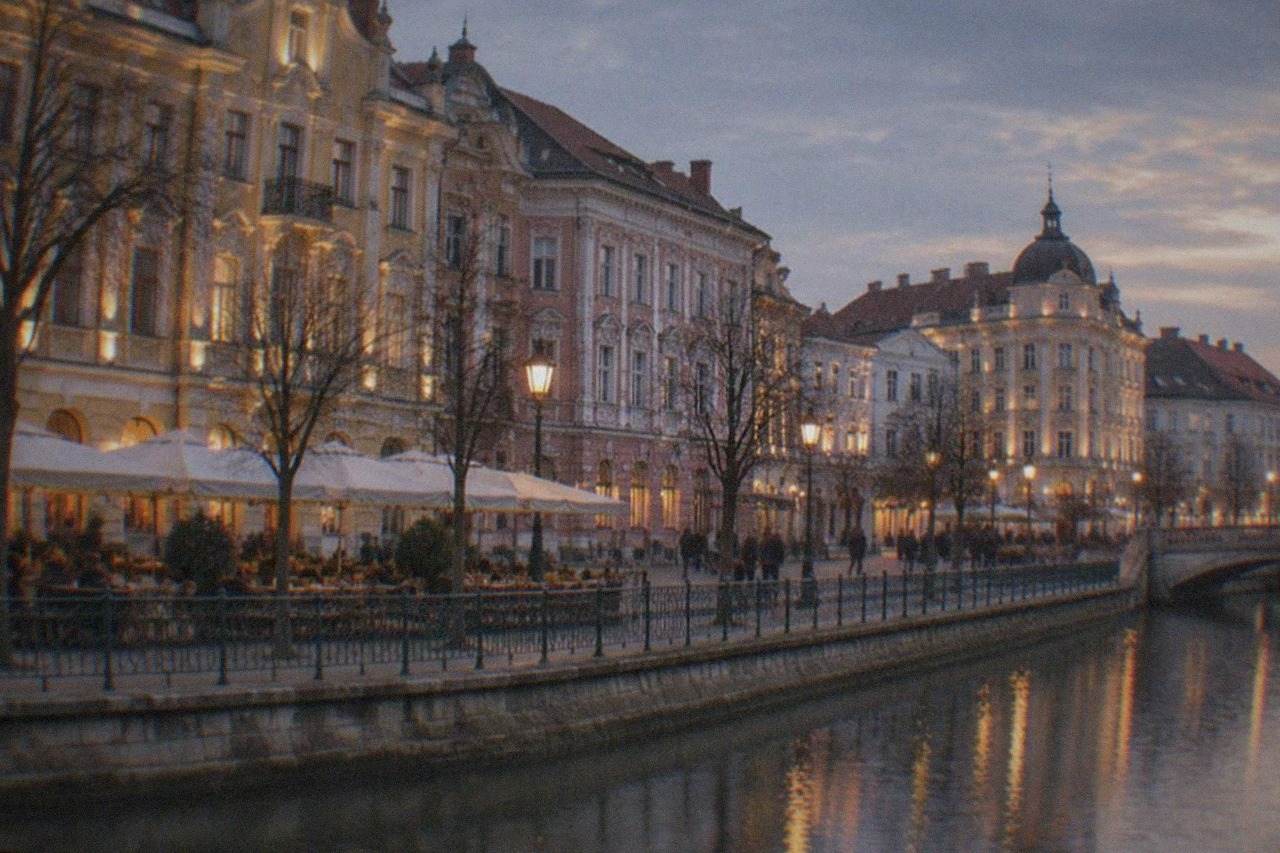 A historic square in Timisoara at dusk with lit baroque facades and outdoor cafe tables