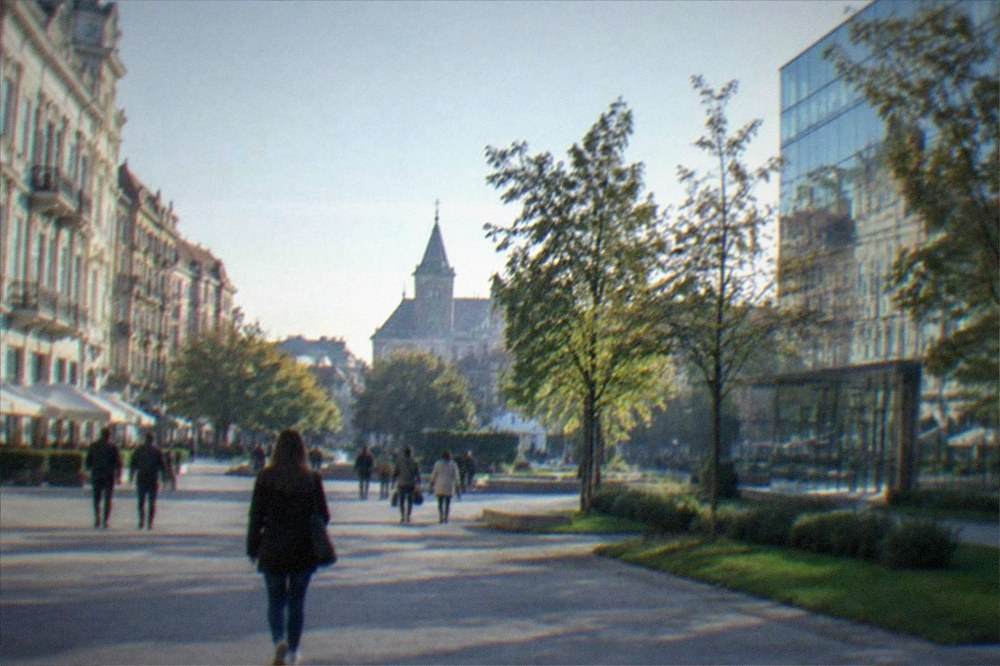People walking through a large modern shopping district with glass buildings and green landscaping