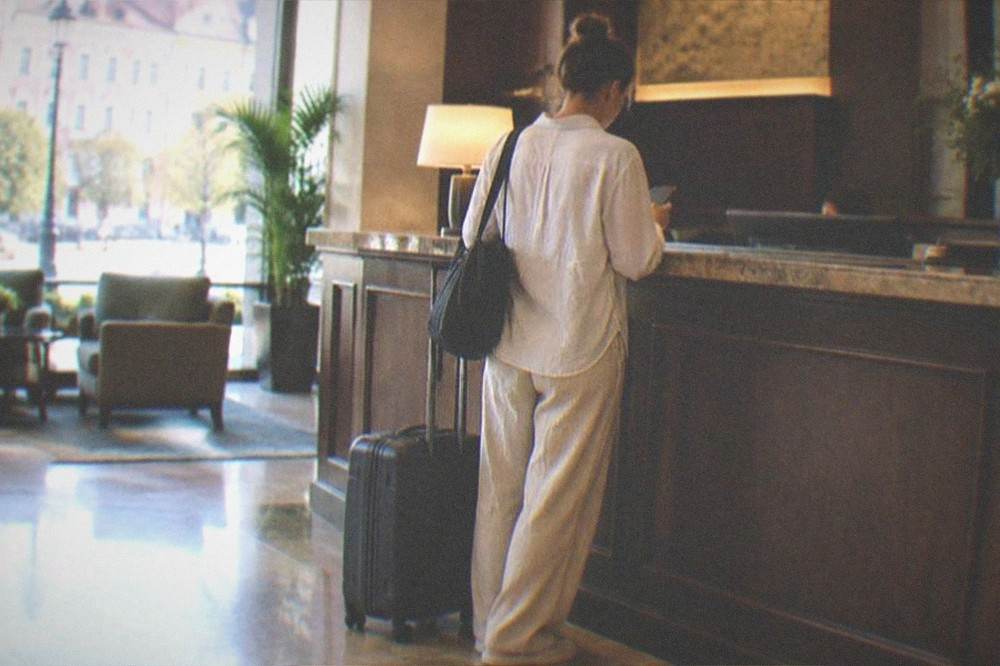 A traveler checking a phone at a hotel reception desk with luggage beside them