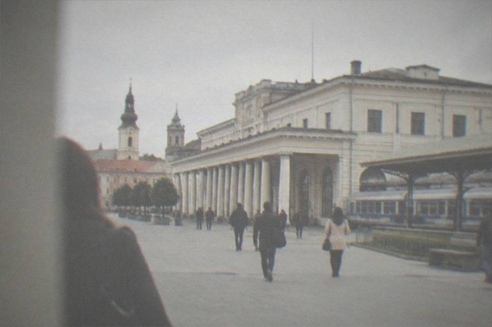 People strolling past pastel-colored buildings and church towers in a historic square