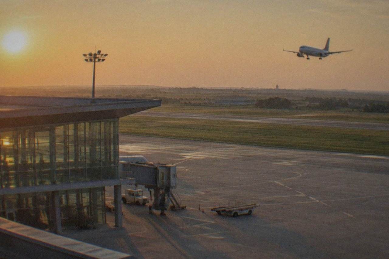 A passenger aircraft descending over green plains toward an airport runway at golden hour