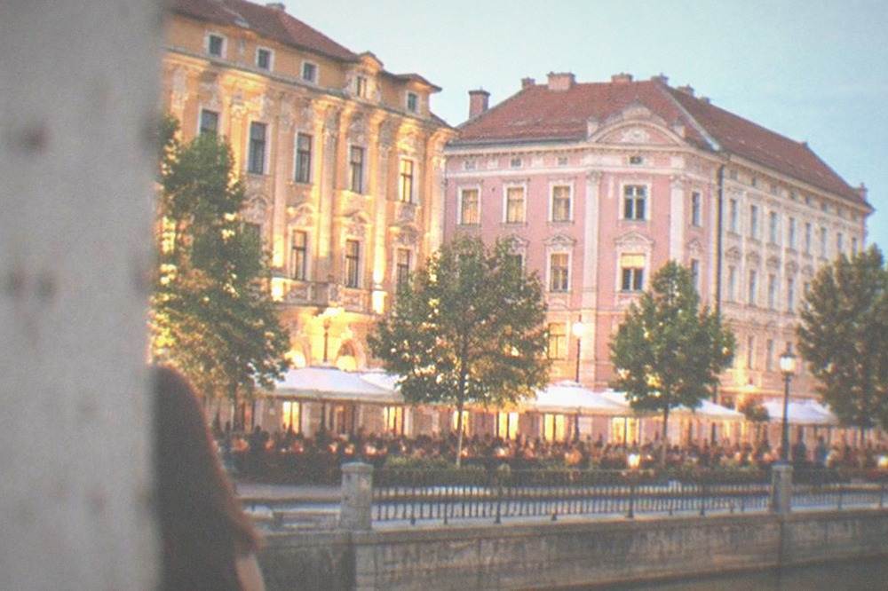Illuminated historic buildings around a Timisoara square at night with people at outdoor tables
