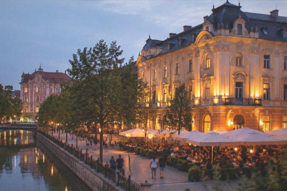 An evening view of a lit historic building and people at an outdoor terrace