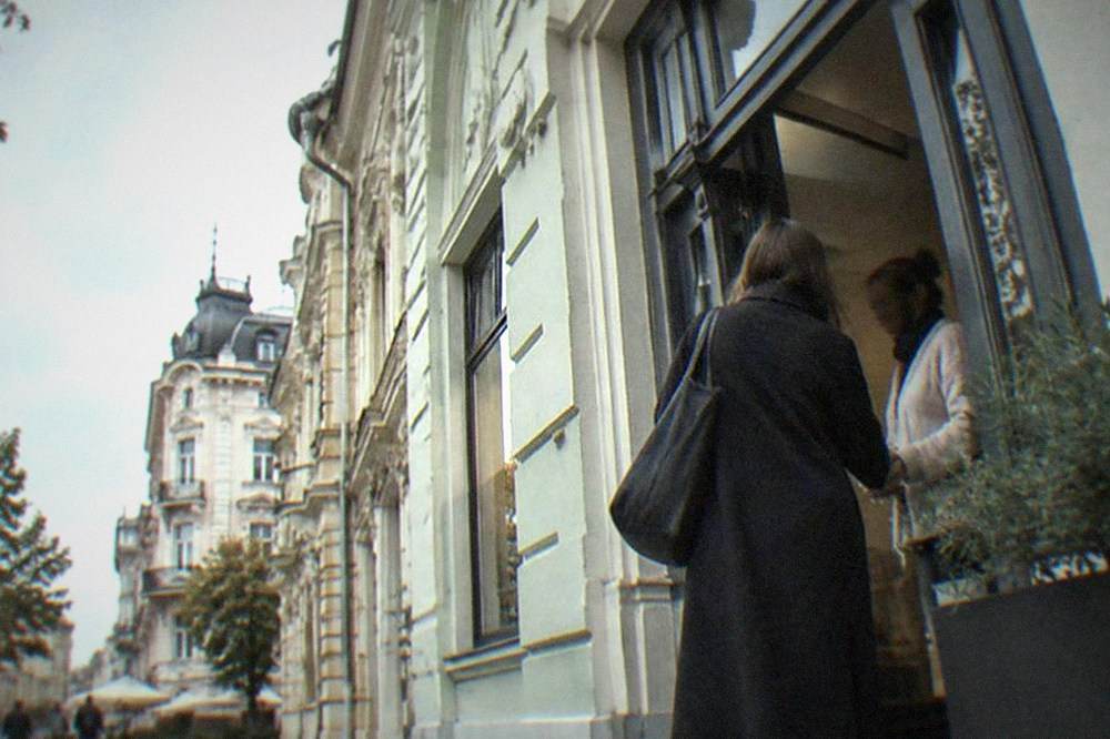 Two people greeting each other at the door of a shop on an old town street