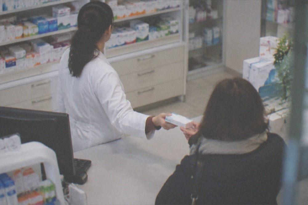 A pharmacist handing a small box over the counter of a pharmacy in Timisoara