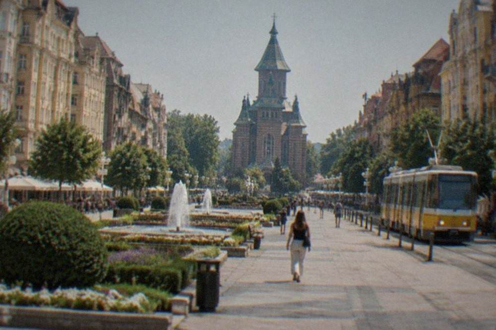 A wide city square lined with colorful buildings and a tram passing through
