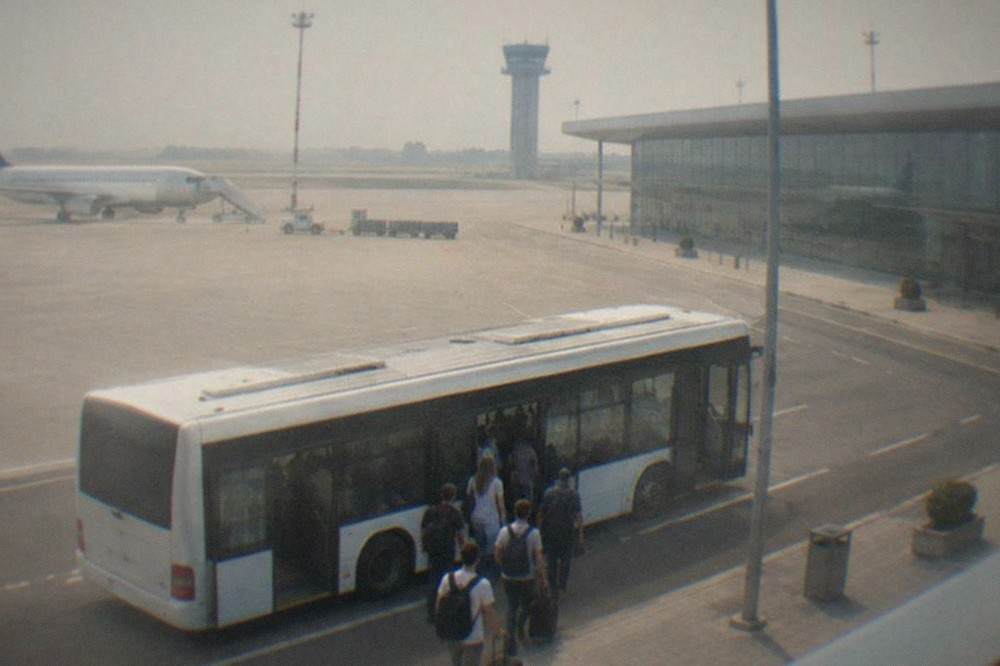 A city bus parked at an airport curb with passengers boarding