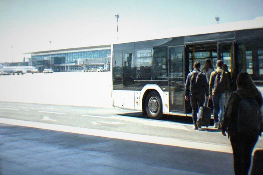 A modern city bus waiting at an airport curb with passengers boarding