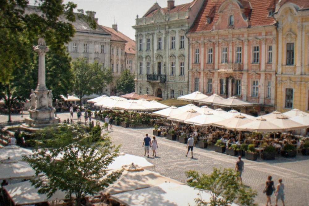 A historic city square in summer with colorful baroque facades and cafe umbrellas