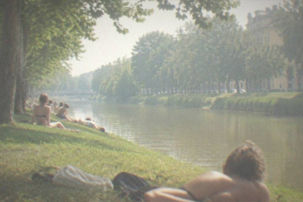 Sunbathers on a grassy bank of the Bega canal on a warm summer afternoon