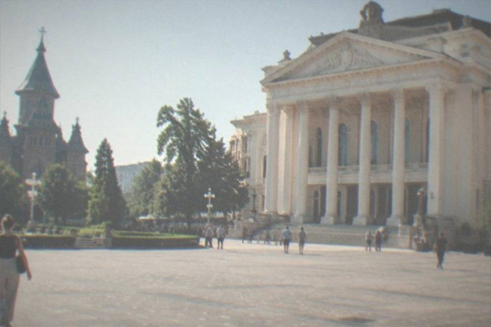A wide city square in Timisoara with a cathedral and opera house on opposite sides
