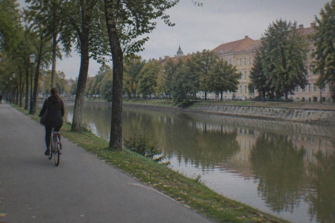A cyclist riding a city bike along a tree-lined path beside a canal in a European city