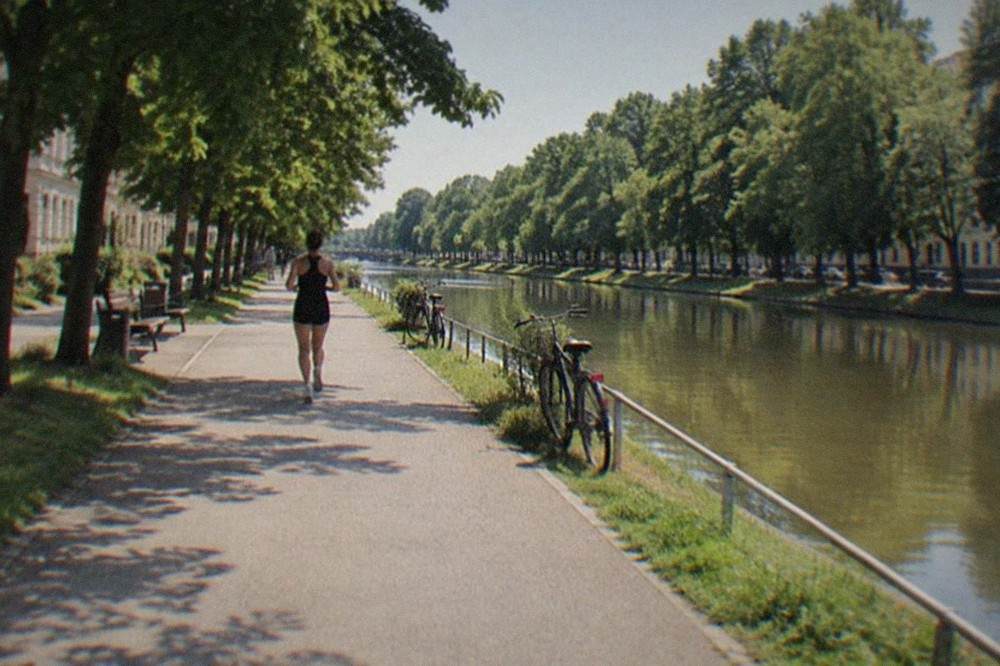 A wide paved path running beside a canal with parked bicycles and green trees on both banks