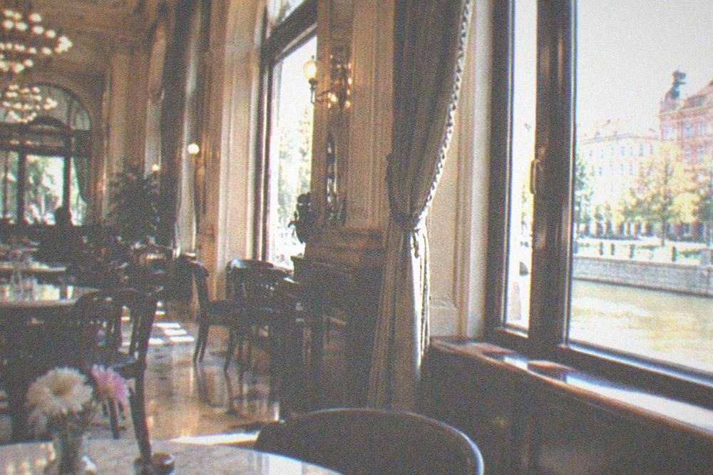 An ornate historic coffeehouse interior with high ceilings, chandeliers and marble tables in Timisoara