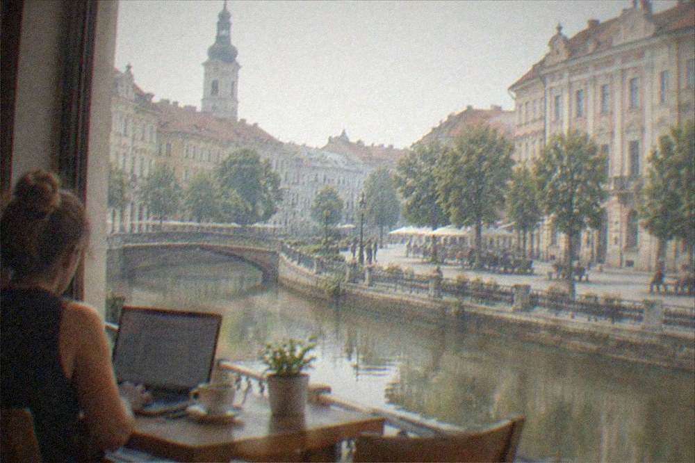 A remote worker with a laptop and coffee at a wooden table by a window in a Timisoara cafe