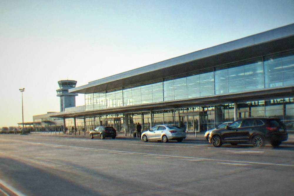 A modern airport terminal building with cars waiting at a pickup curb outside