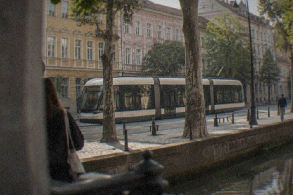 A modern tram passing colorful buildings on a tree-lined street in Timisoara