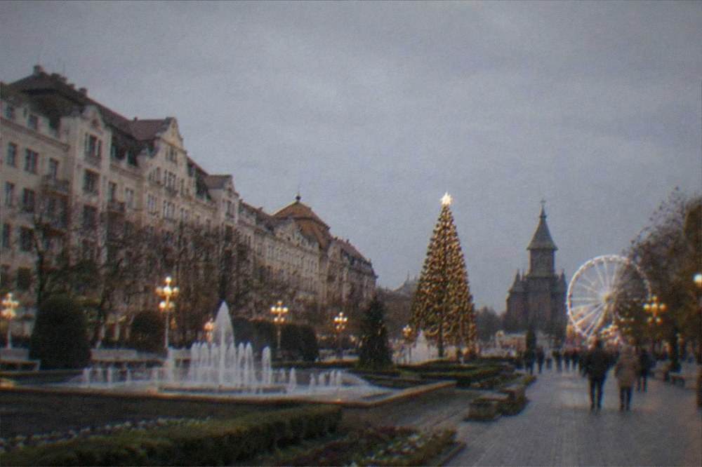 Illuminated Christmas tree and ferris wheel lights above a city square at night