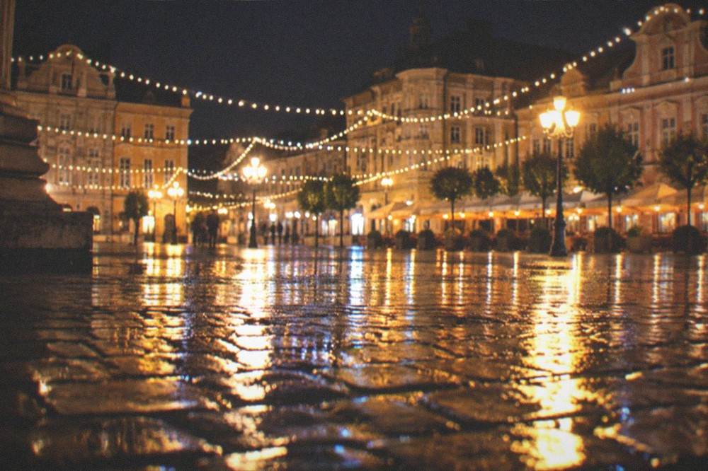 Festive lights reflecting on wet cobblestones in an old town square at night