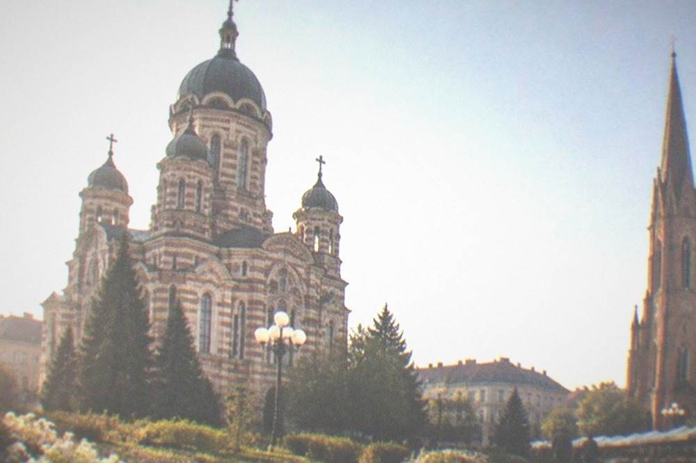 Tall Neo-Gothic spire of a brick parish church above a neighborhood square with market stalls