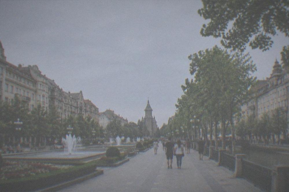 People strolling along a tree-lined city promenade beside a canal in warm weather