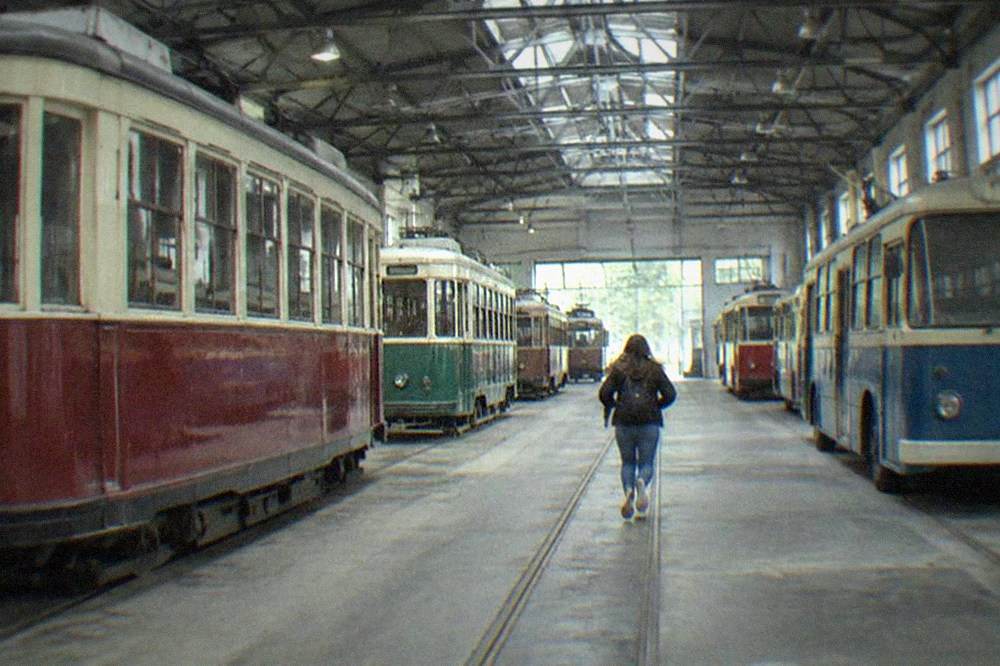 A vintage tram moving down a tree-lined street beside old European buildings