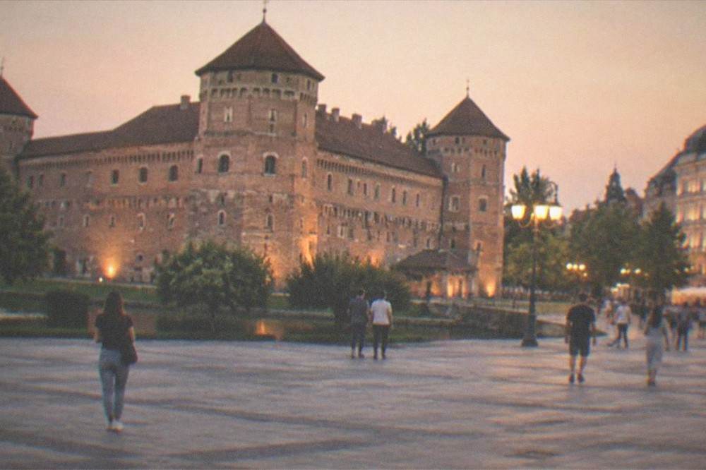 A wide city square at dusk with lit facades and people walking