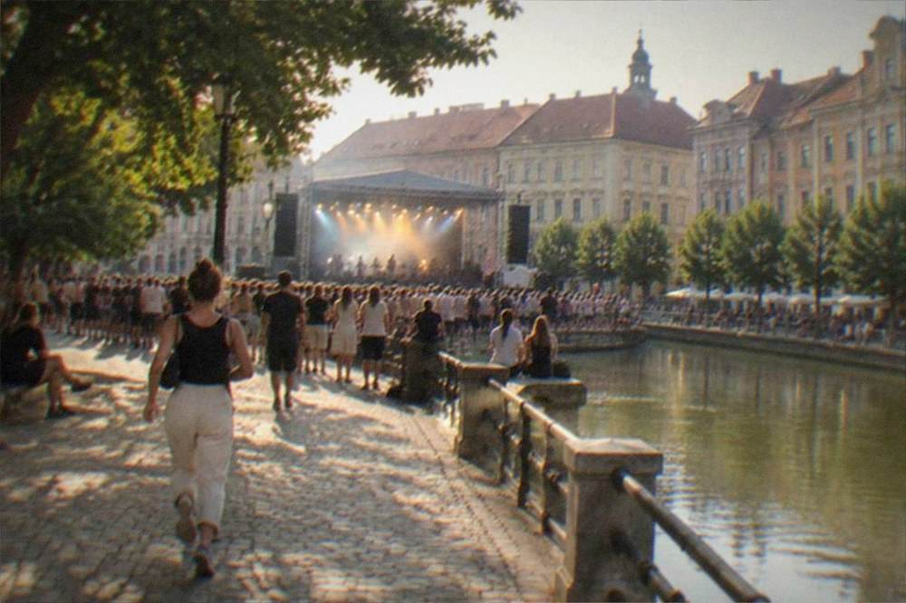 People gathered at an outdoor evening concert in a Timisoara square with lit stage lights