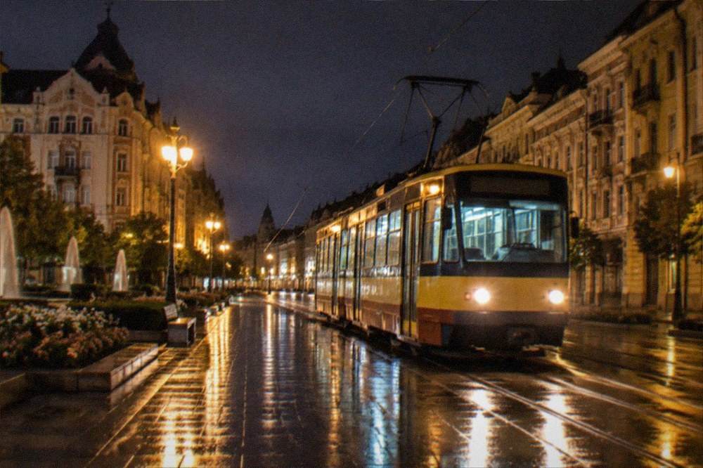Empty lit city street at night with a tram passing and wet pavement reflections