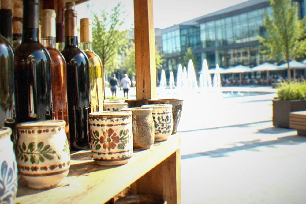 Bottles of local Banat wine and handmade ceramic cups arranged on a wooden shop shelf